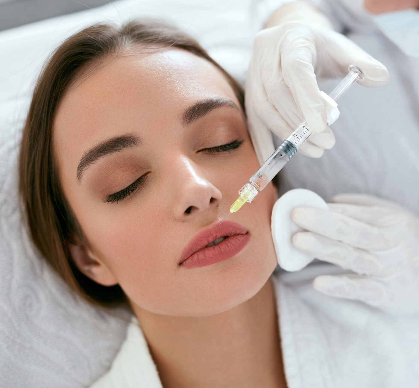 A gloved injector holding a syringe beside a client's cheek, the client's eyes closed