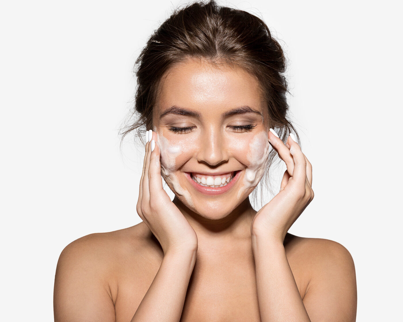 A smiling woman cleansing her face with a foaming cleanser